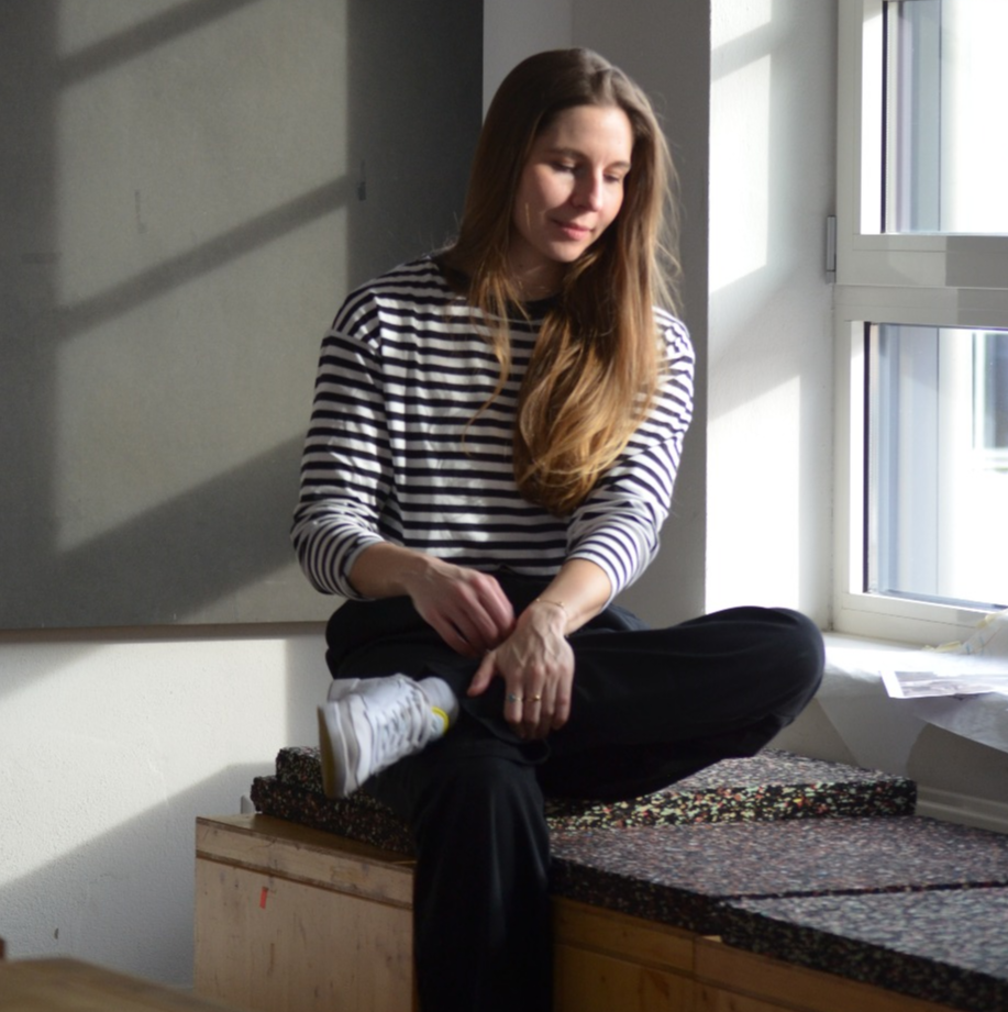 Andréa Hugen sitzt auf einer Holzkiste vor dem Fenster und schaut nach unten..