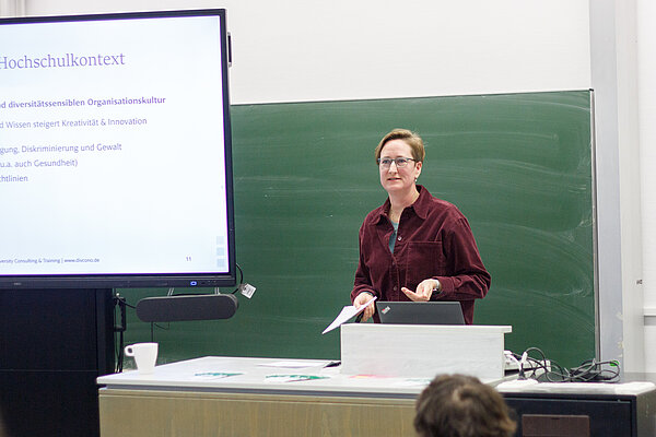 Keynote speech by Dr. Steffi Nothnagel In the picture, Dr Steffi Nothnagel stands behind a lectern and speaks to the audience. Next to her is a screen showing her presentation.