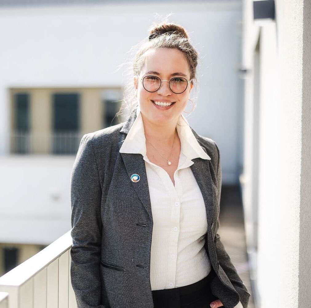 Auf dem Bild steht Susann Resmer an ein Geländer gelehnt vor einem Gebäude.