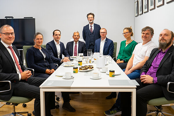 Neuberufene Profs. Okt. 2025 mehrere Personen sitzen als Gruppe an einem Tisch und lächeln in die Kamera