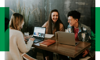 Drei Frauen sitzen zusammen am Tisch und sind miteinander im Gespräch. Vor ihnen stehen Laptops, Bücher und Getränke.