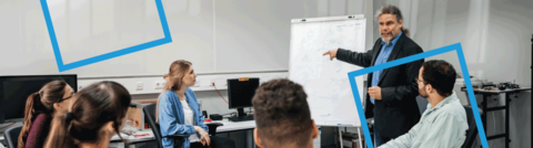 Hochschuldidaktik_Zusatz Das Bild zeigt einen Banner. In Hintergrund ist ein Mann mit langen Haaren und Anzug zu sehen, der Studierenden etwas auf einem Flipchart erklärt.