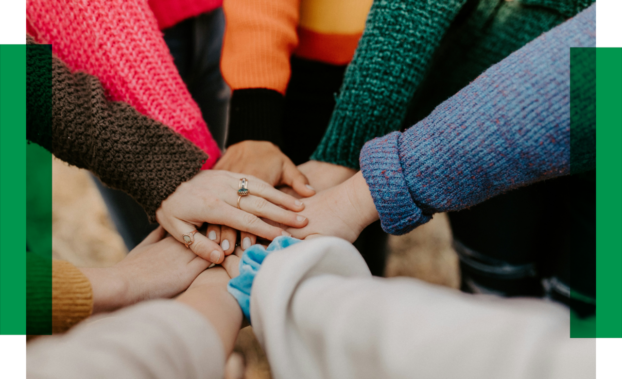 People stand in a circle and put their hands together in the middle. These clasped hands are in the center.