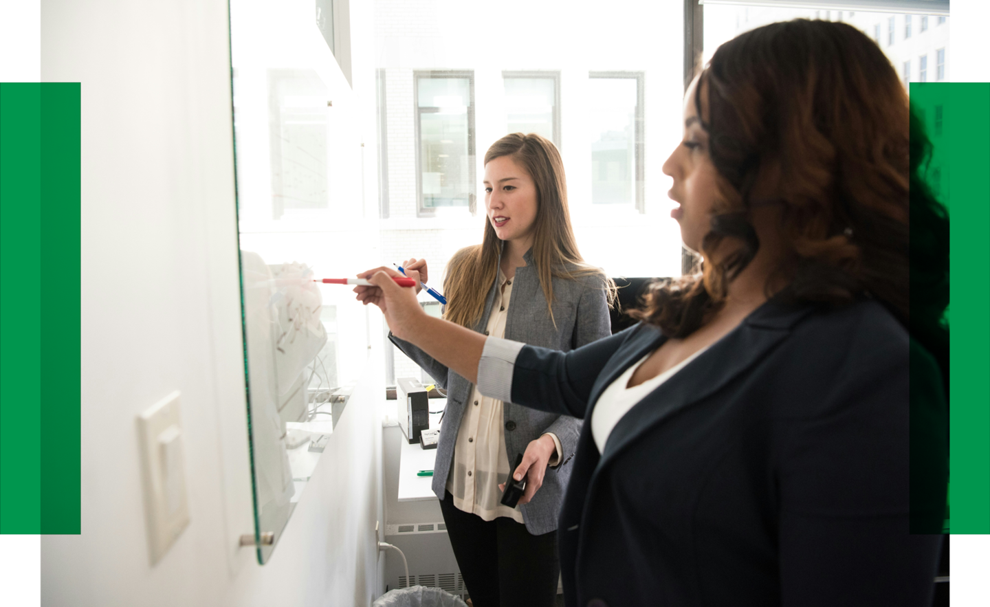 Zwei Frauen stehen vor einem Whiteboard und schreiben darauf.