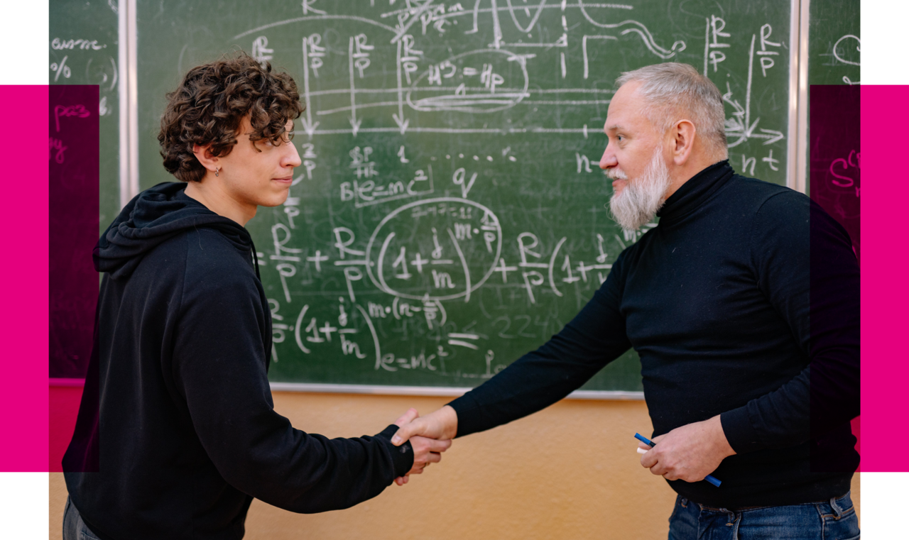 The image shows two people in a classroom shaking hands. The person on the left is a young man with curly hair, looking to the right and wearing a dark hoodie. The person on the right is an older man with a gray beard, smiling and looking to the left while holding the younger man's hand. He is wearing a black turtleneck sweater and holding a blue marker in his other hand. Behind them is a chalkboard filled with complex mathematical formulas and diagrams written in chalk. On the left side of the image, there is a magenta bar, possibly part of a graphic design.