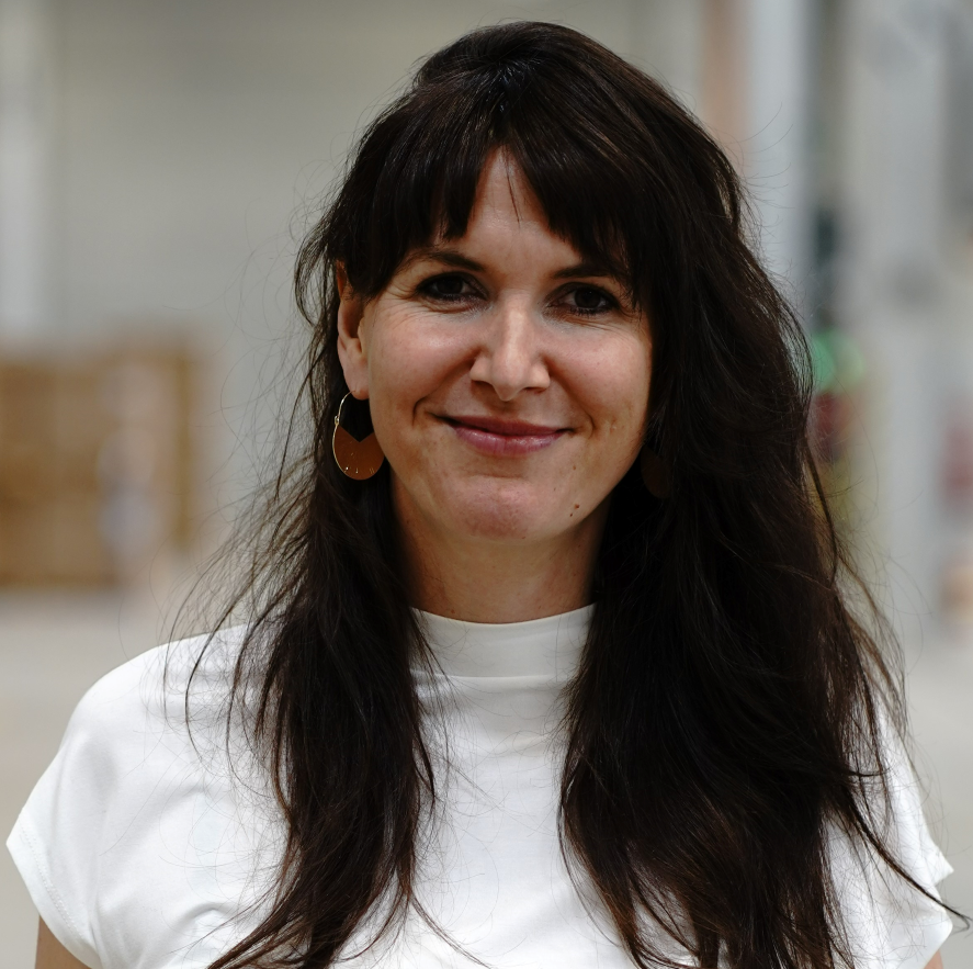 Portrait mit Oberkörper von Anna Förster. Sie steht in einer Lagerhalle.