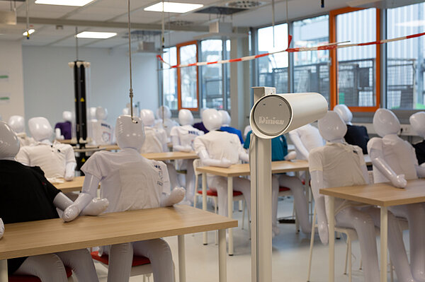 In einem Klassenraum sitzen aufblasbare Puppen mit T-Shirts an Tischen