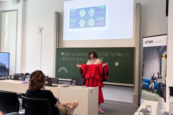 Eine Person steht vor einer Tafel und hält einen Vortrag vor Publikum.