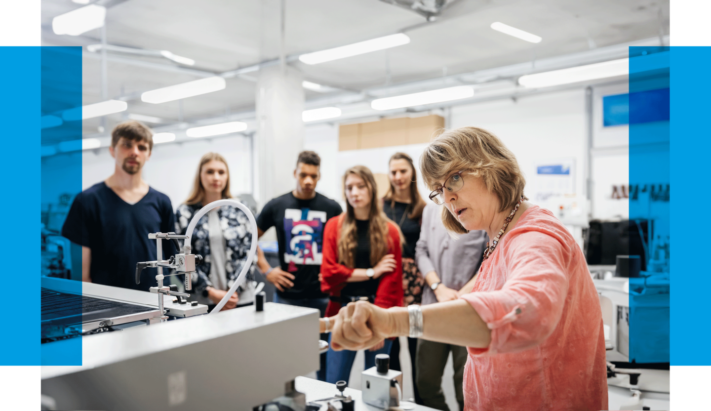 Teilen Sie Ihren Erfahrungsschatz mit der nächsten Generation! Eine Professorin erklärt Studierenden eine Druckmaschine. Dazu steht dort geschrieben: "Gestalten Sie die Zukunft mit!"