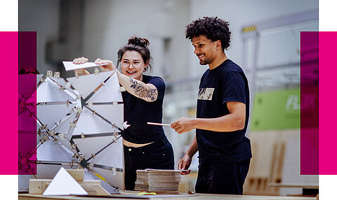 Lächelnd am Architekturmodell Zwei junge Personen arbeiten lachend an einem geometrischen Modell aus weißen, dreieckigen Elementen auf einem Werkstatttisch.