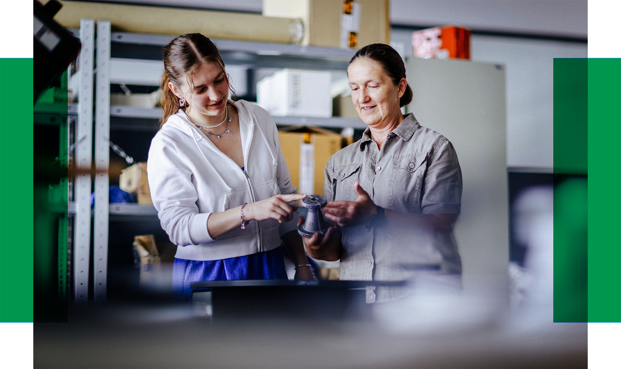Zwei Frauen in einem Lagerraum betrachten gemeinsam ein technisches Bauteil und besprechen es.